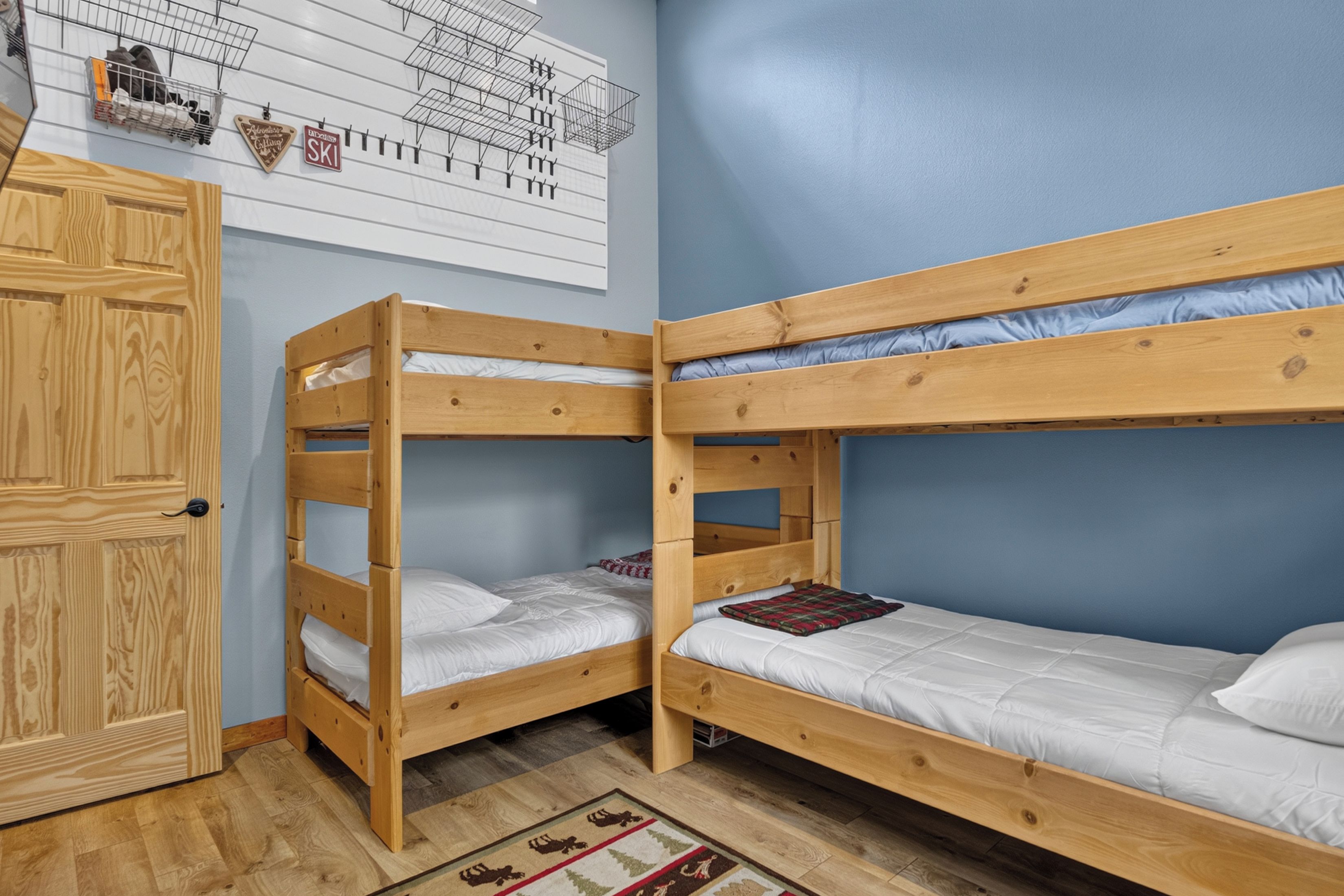 A room with two bunk beds, a wooden wardrobe, and a wall with a ski-themed decoration.