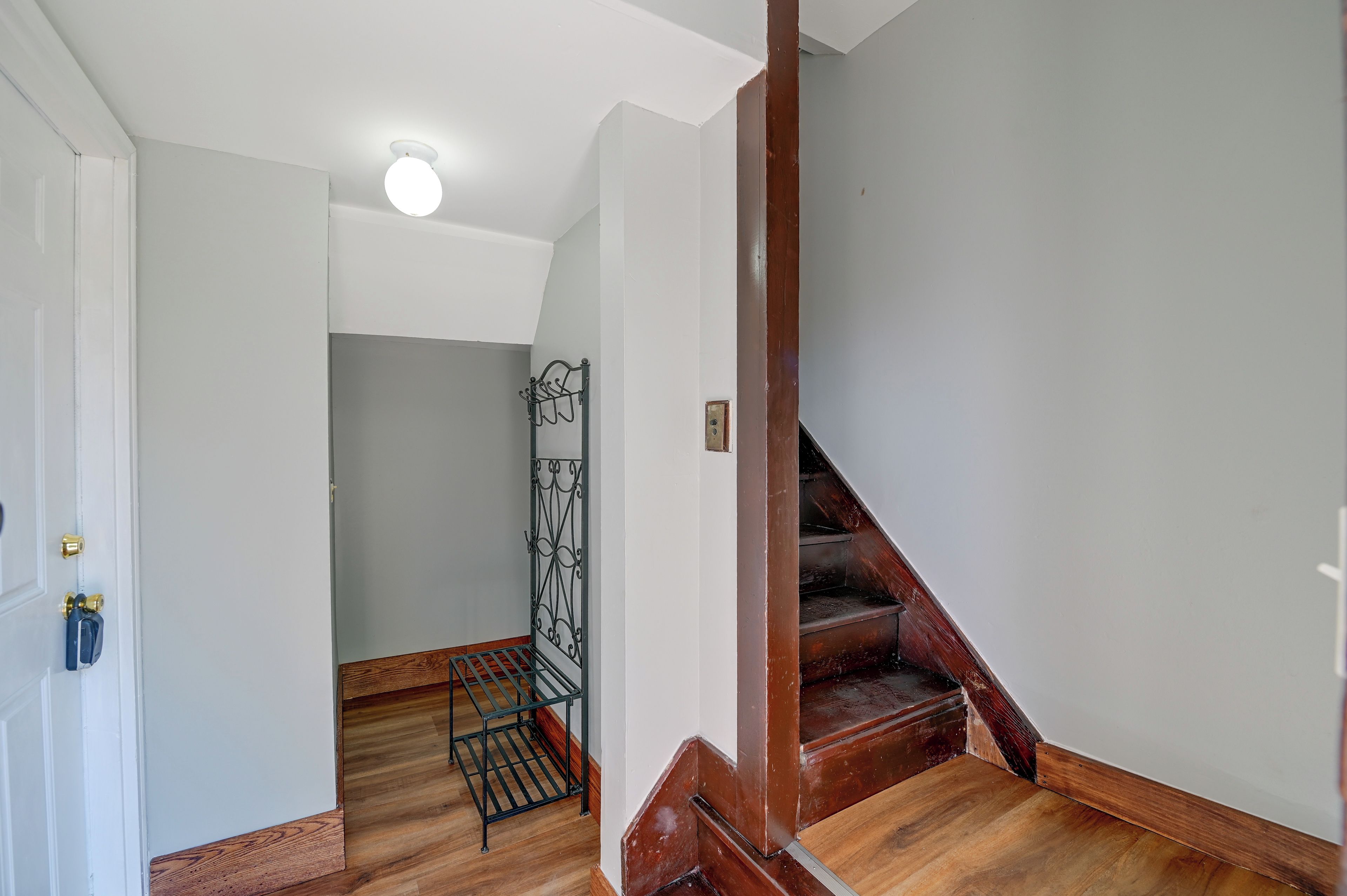 A hallway with a wooden staircase, a metal gate, and a white door.