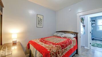 A bedroom with a bed, a bedside table with a lamp, a framed picture on the wall, and a door leading to another room.