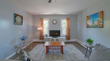 A living room with a television, a clock, and a painting of the Eiffel Tower.