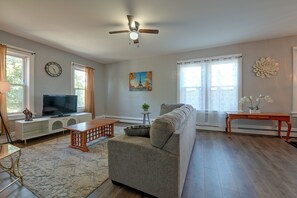 A living room with a sofa, a TV, a ceiling fan, and a painting of the Eiffel Tower.