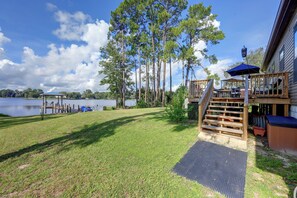 A lakeside deck with a wooden staircase leading to a covered seating area, a dock with chairs, and a grassy lawn. - Waterfront Interlachen Retreat w/ Dock on Lake Ida (Interlachen)