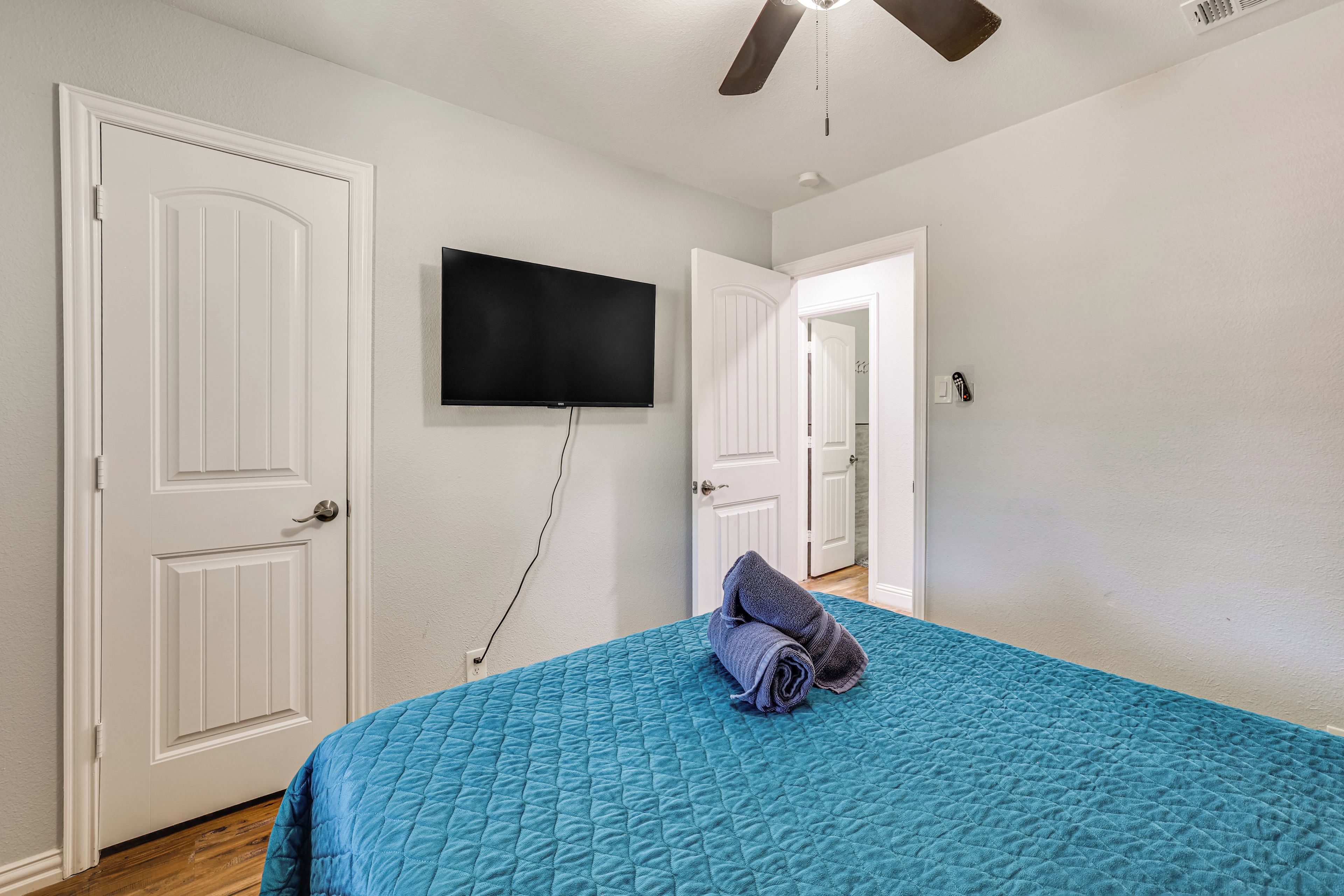 A bedroom with a bed, a television mounted on the wall, and a ceiling fan.