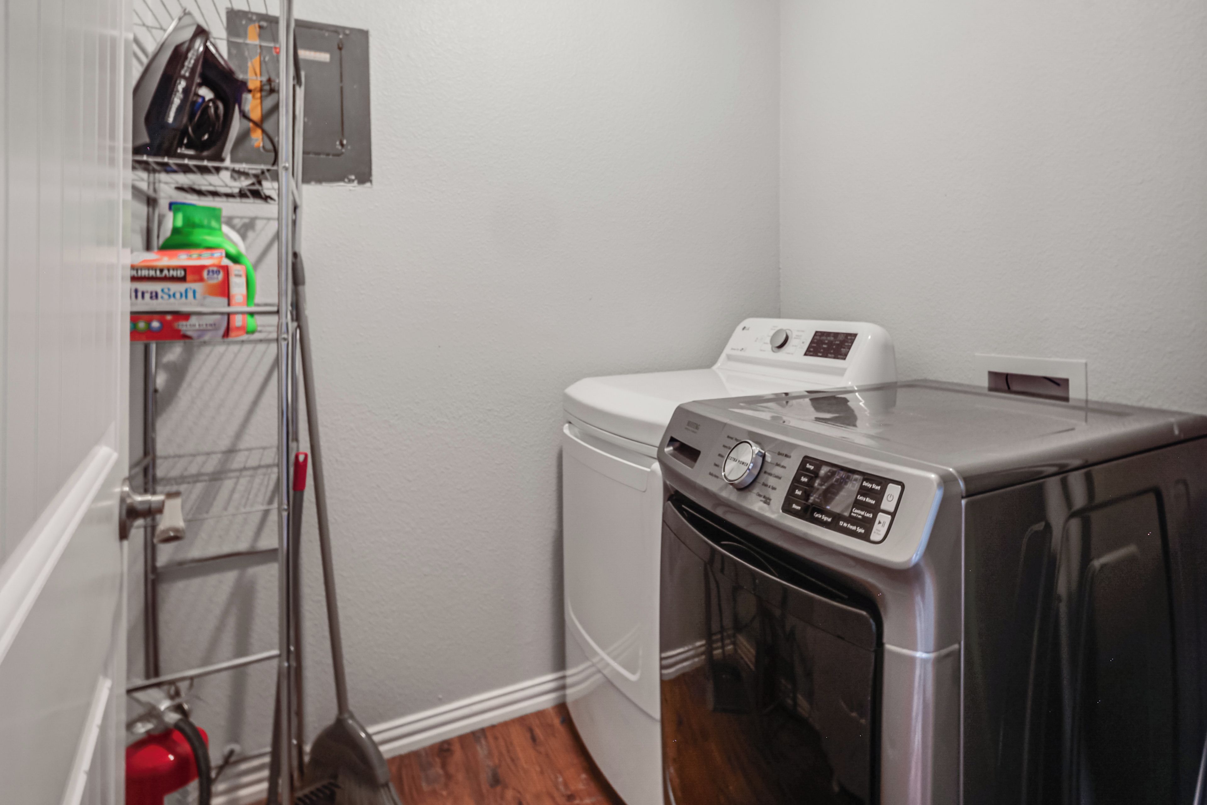 A laundry room with a washing machine, dryer, and a shelf with cleaning supplies.