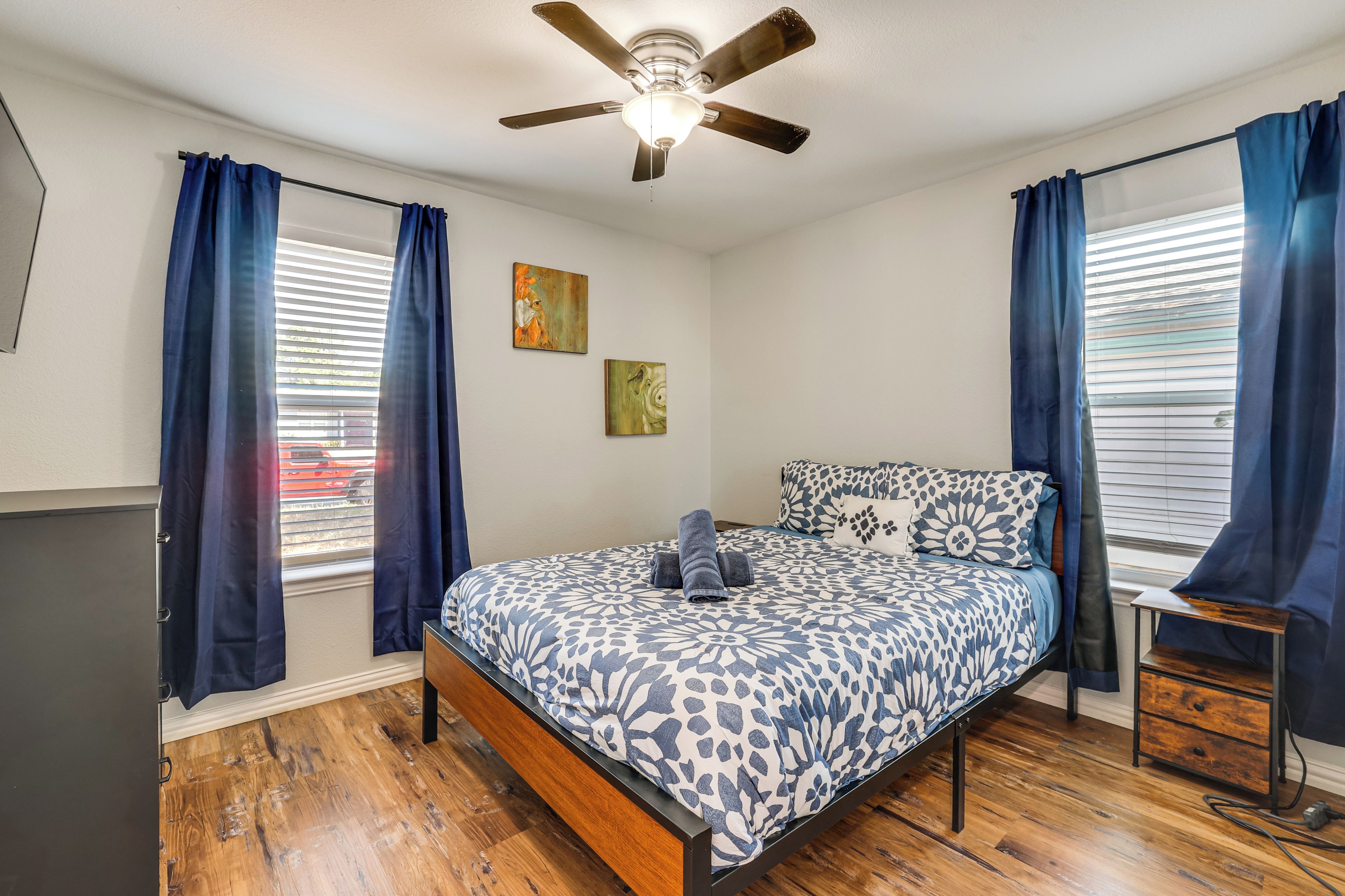A bedroom with a bed, a ceiling fan, and two windows with curtains.