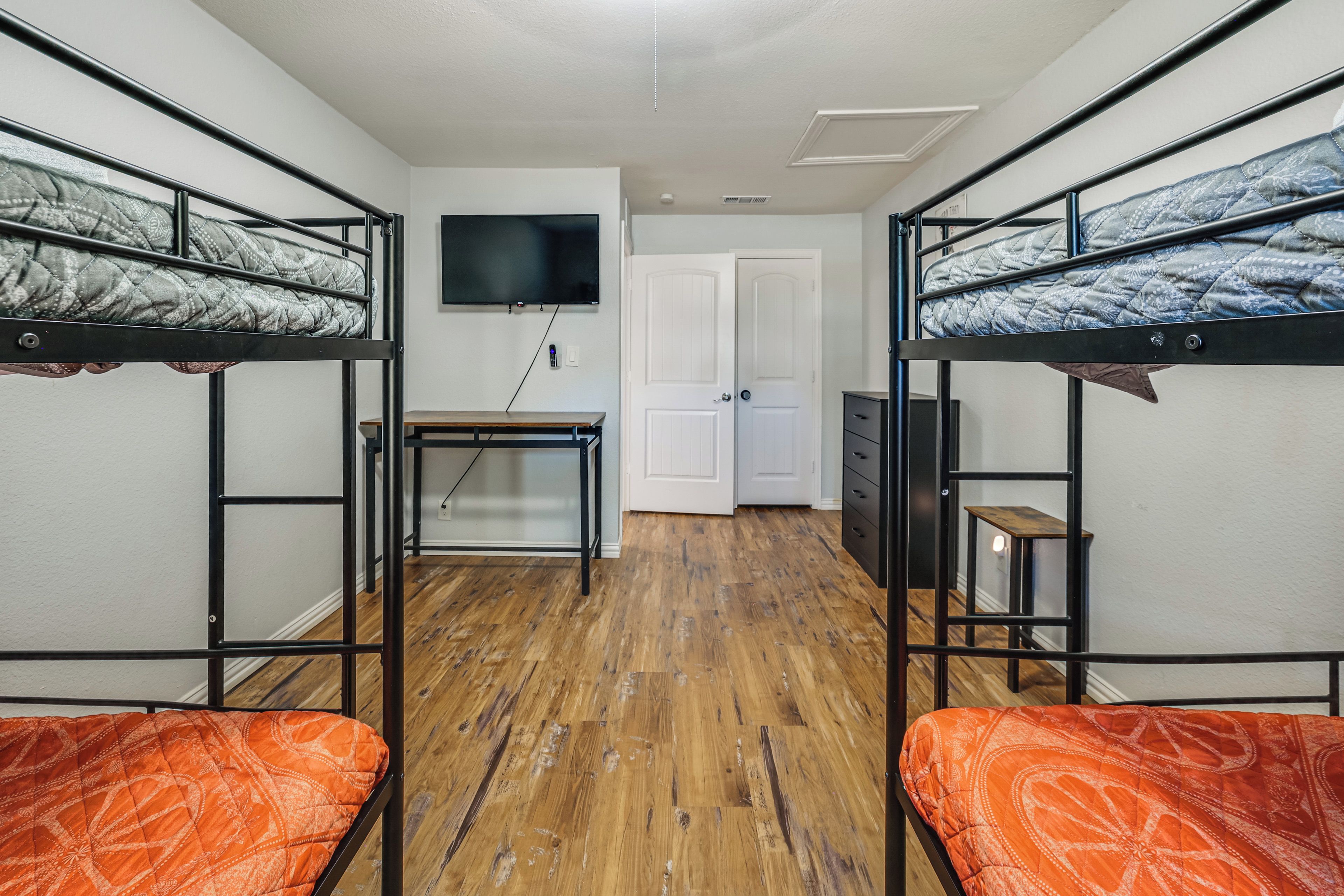 A dormitory room with bunk beds, a desk, a television, and a door.