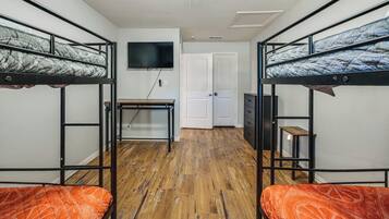 A dormitory room with bunk beds, a desk, a television, and a door.