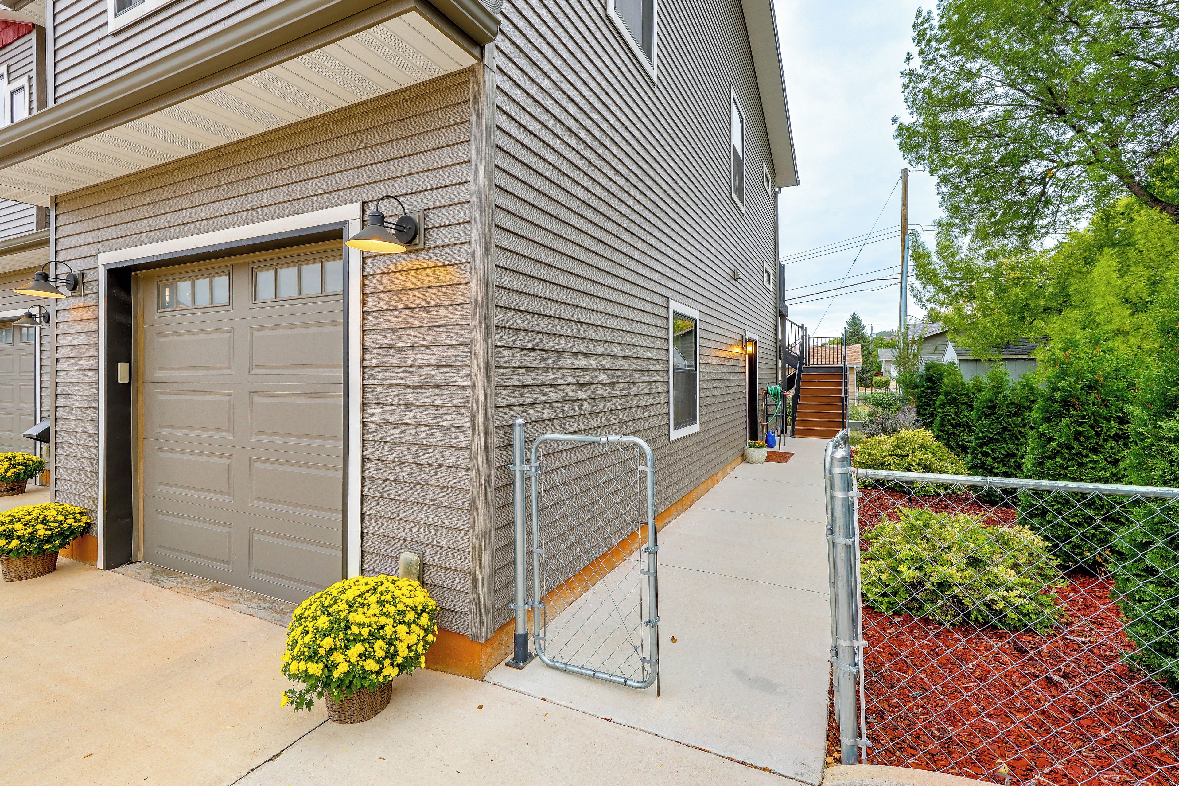 A residential garage with a metal gate, a concrete driveway, and yellow flowering plants.