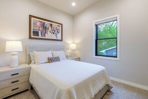 Un dormitorio con cama, dos mesitas de noche, un velador, una ventana y un cuadro en la pared.