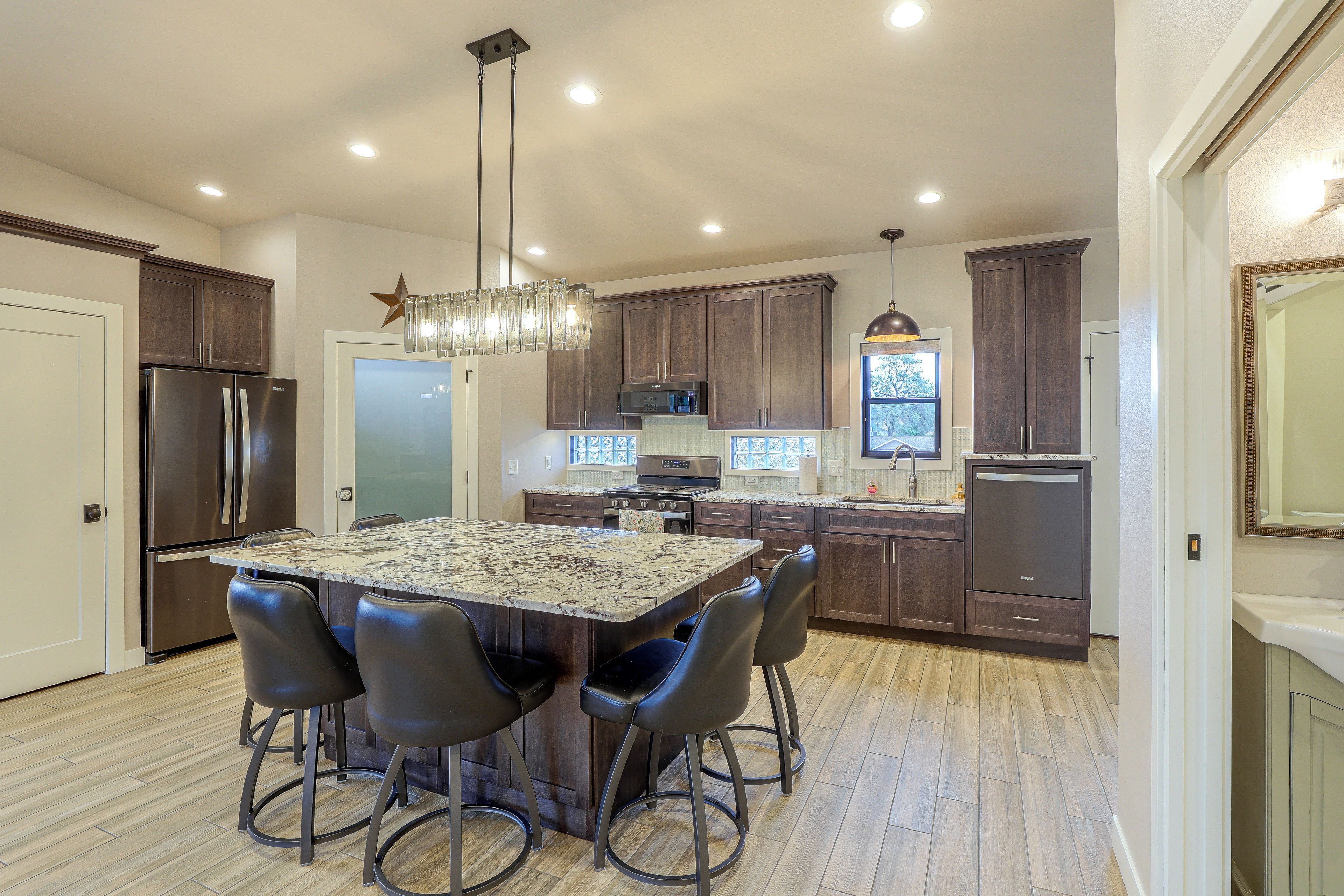 A modern kitchen with a central island, dark wooden cabinets, stainless steel appliances, and a pendant light fixture.