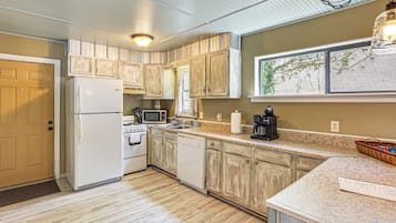 A kitchen with white appliances, wooden cabinets, a granite countertop, and a window with a view.