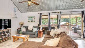 A spacious living room with a ceiling fan, a television, and a large window with curtains.