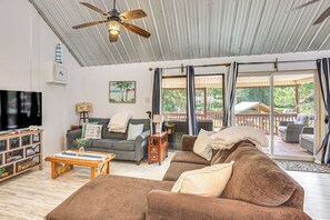 A spacious living room with a ceiling fan, a television, and a large window with curtains. - Fish & Hunt! Waterfront Home w/ Dock in Midway (Midway)