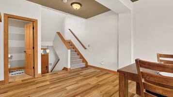 A room with a wooden floor, a staircase, a dining table with chairs, and a door leading to a bathroom.