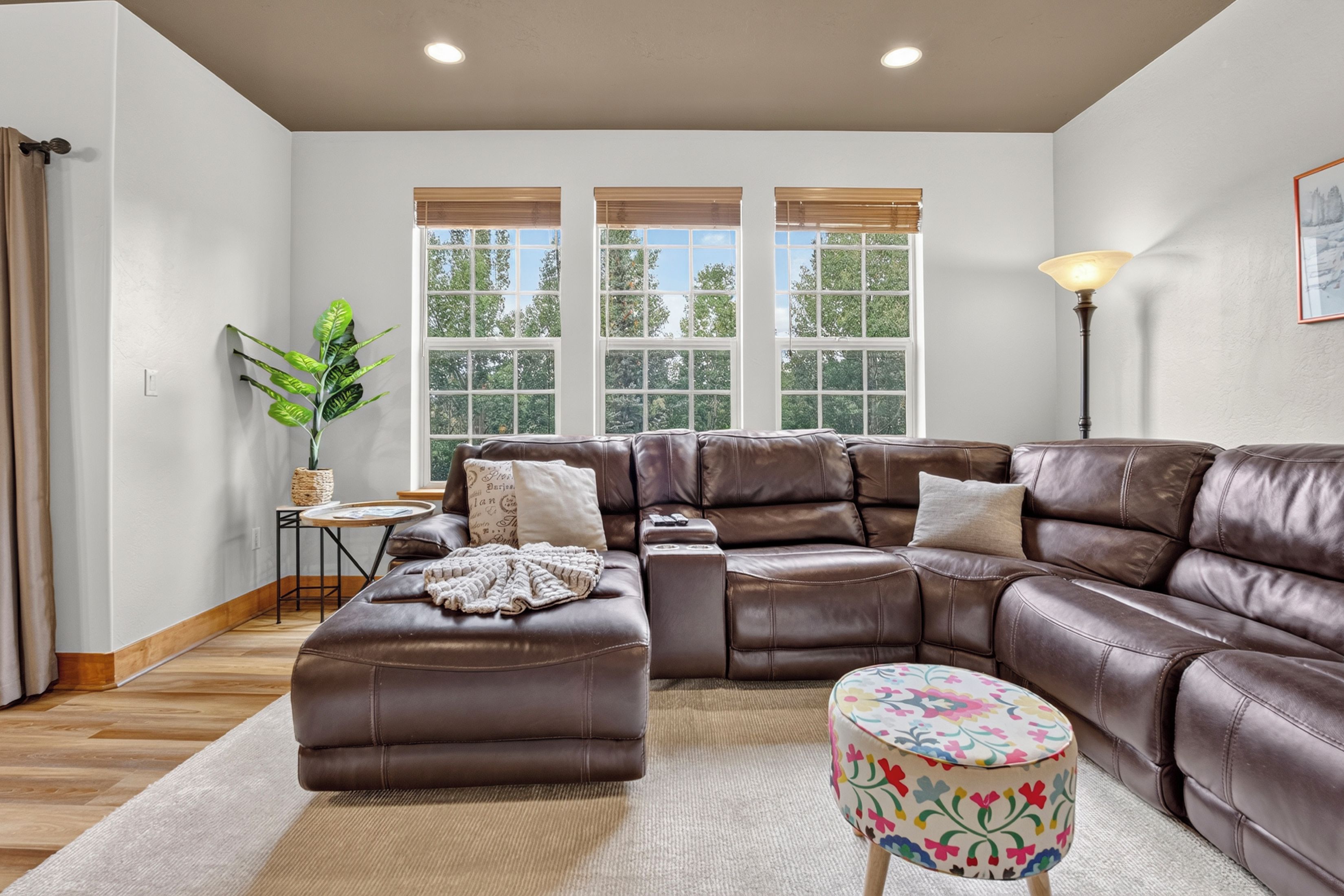 A modern living room with a sectional sofa, a small round ottoman, and a side table with a plant.