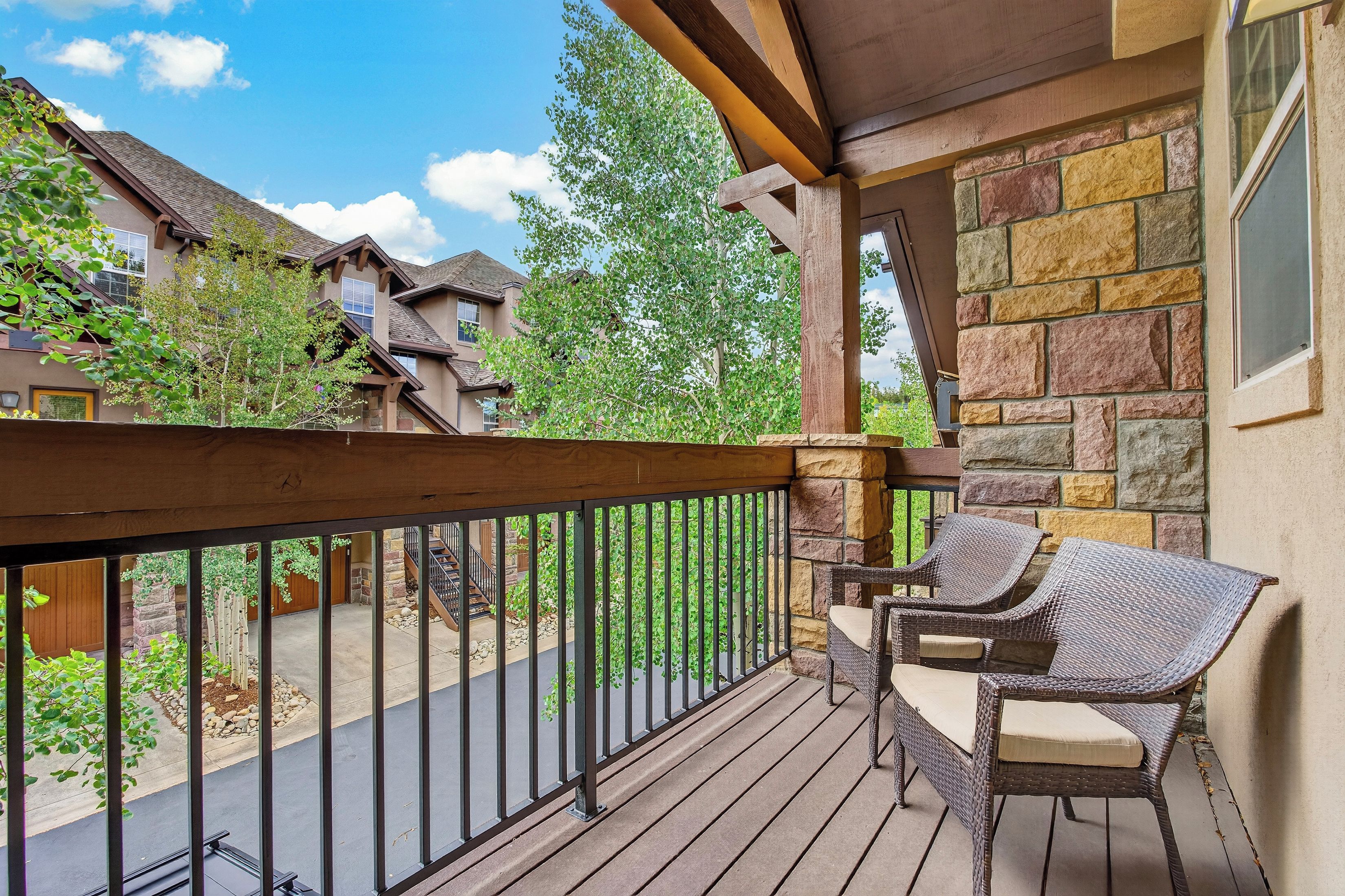 A wooden deck with a wicker chair, stone wall, and a view of neighboring houses.