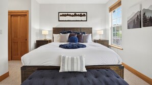 Een slaapkamer met een groot bed, twee nachtkastjes, een houten deur en een raam met uitzicht.