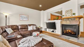 A living room with a brown leather sofa, a flat-screen TV, a fireplace, and a framed picture on the wall.