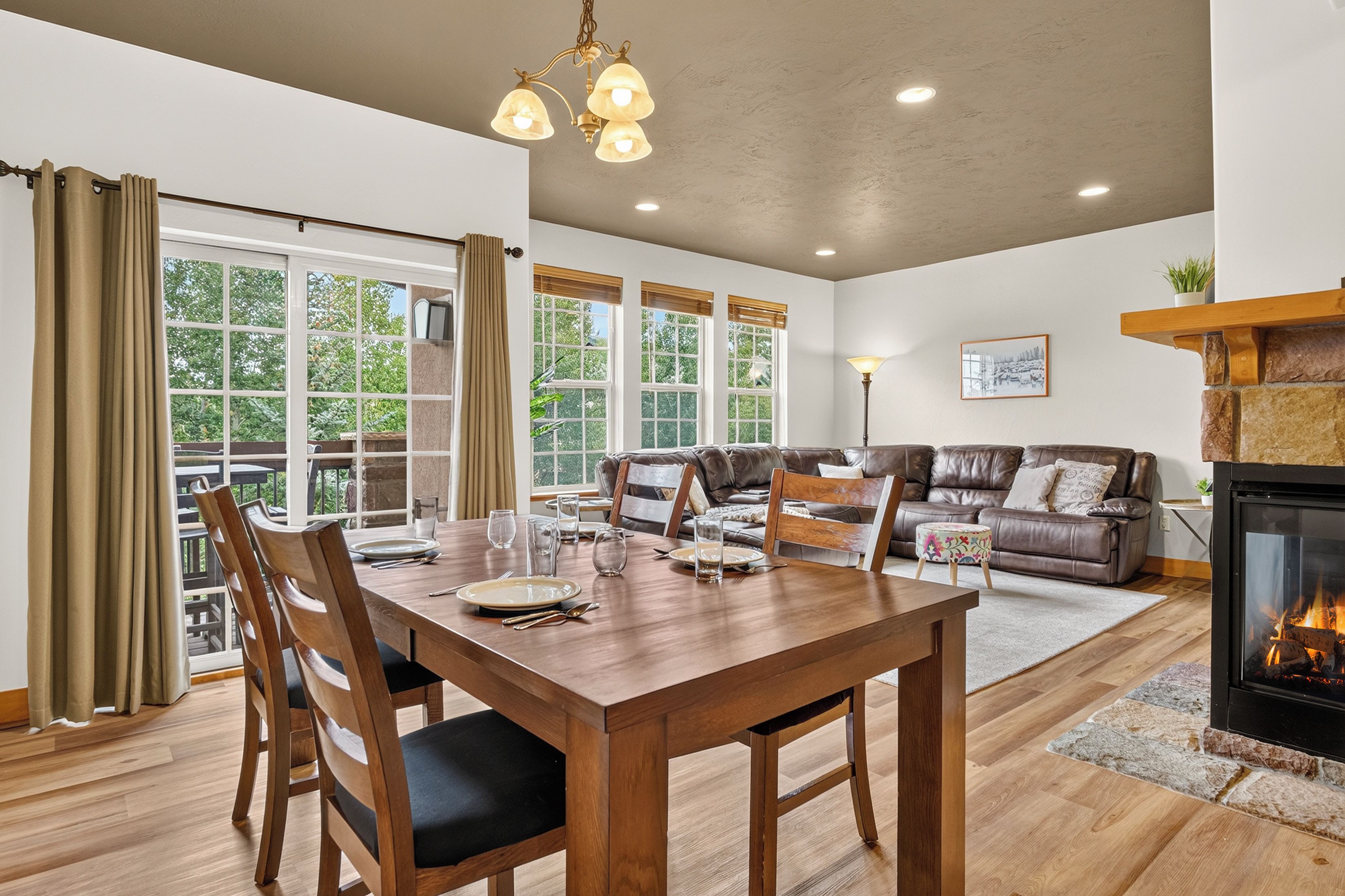 A dining area with a wooden table and chairs, a fireplace, and a view of the outdoors through large windows.