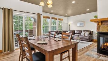A dining area with a wooden table and chairs, a fireplace, and a view of the outdoors through large windows.