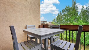 Een balkon met een tafel en twee stoelen, met uitzicht op een woonwijk met bomen en een heldere lucht.