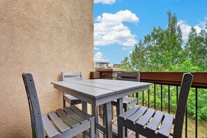Un balcón con una mesa y dos sillas, con vistas a una zona residencial con  árboles y un cielo despejado.