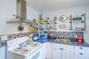 A kitchen with a stove, microwave, and sink. There are shelves with decorative items and a sign that says 'WELCOME to our Airbnb.' - Corner Cottage - Just Minutes From the Water (Aransas Pass)