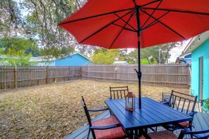 Eine Terrasse mit Tisch, Stühlen und einem roten Sonnenschirm, umgeben von einem Holenzaun.