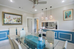 A dining area with a glass table, white chairs, a ceiling fan, pendant lights, and artwork on the walls. - Hidden Gem Near Ocean Center, Water Park & Theater (Daytona Beach)