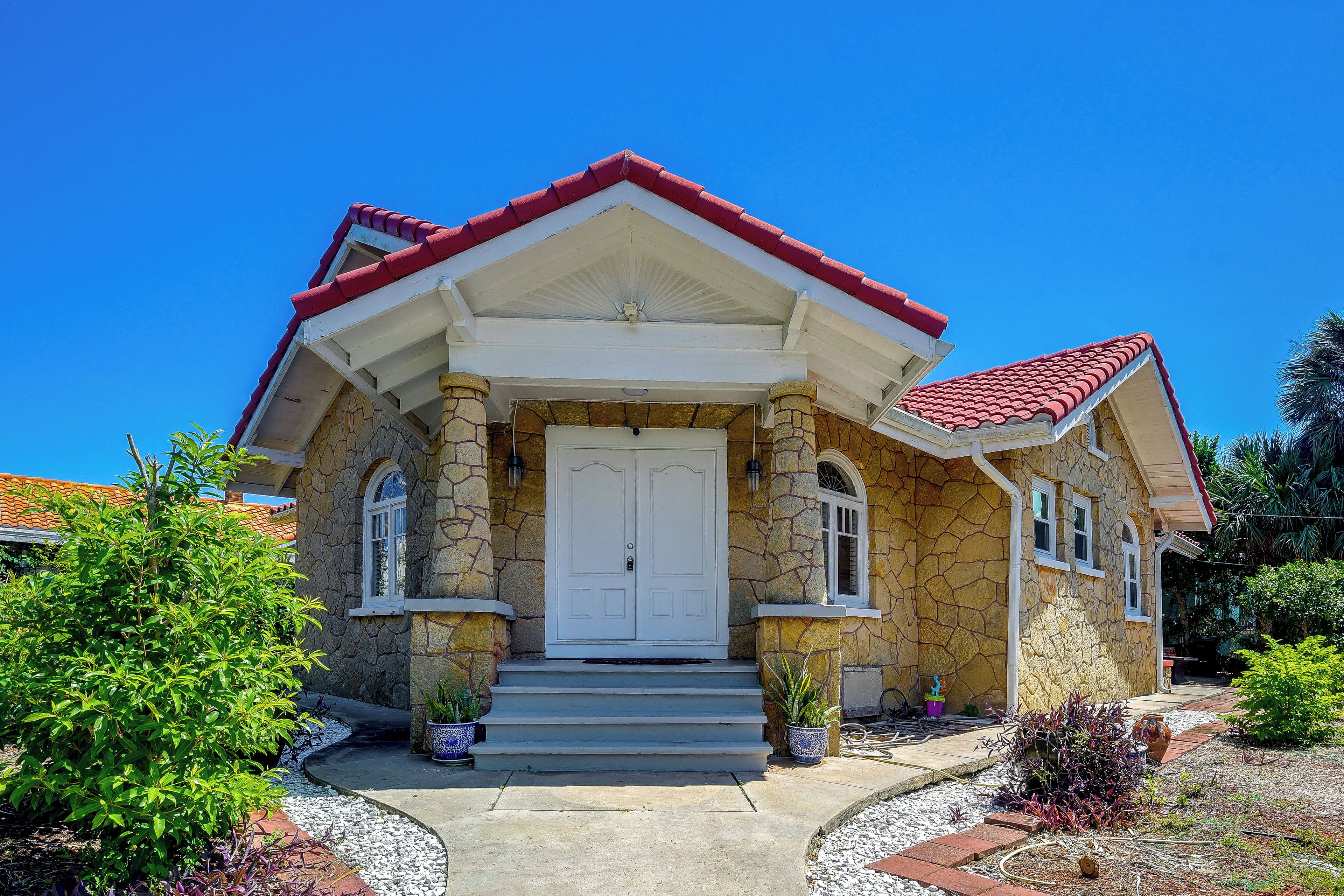 A two-story house with a stone facade, a red-tiled roof, and a white front door.