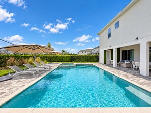 A swimming pool with lounge chairs and a covered area, surrounded by a hedge and a building. - Amazing 9 bedrooms and private pool with spa (Kissimmee)