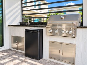 Eine Außenküche mit integriertem Grill, einem schwarzen Kühlschrank und Edelstahl-Schränken.