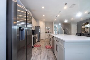 A modern kitchen with stainless steel appliances, a white countertop, and pendant lighting. - Amazing 9 bedrooms and private pool with spa (Kissimmee)
