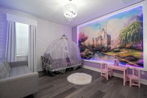Ein Kinderzimmer mit Wandgemälde eines Schlosses, einem Baldaktimbett und einem kleinen Tisch mit Stühlen.
