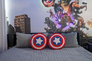 Ein Schlafzimmer mit einem Bett, ausgestattet mit zwei Kissen mit einem Sternemblem, einer Wandmalerei von Superhelden und einer Skyline im Hintergrund.