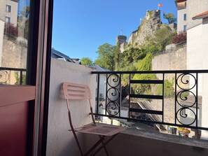Ein Balkon mit einem Metallstuhl, einem schmiedeeisernen Geländer und Blick auf ein historisches Gebäude mit einer Flagge.