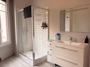 A modern bathroom with a glass-enclosed shower, a white vanity with a mirror, and a tiled floor. - At Julien's - view of the castle (Lourdes)