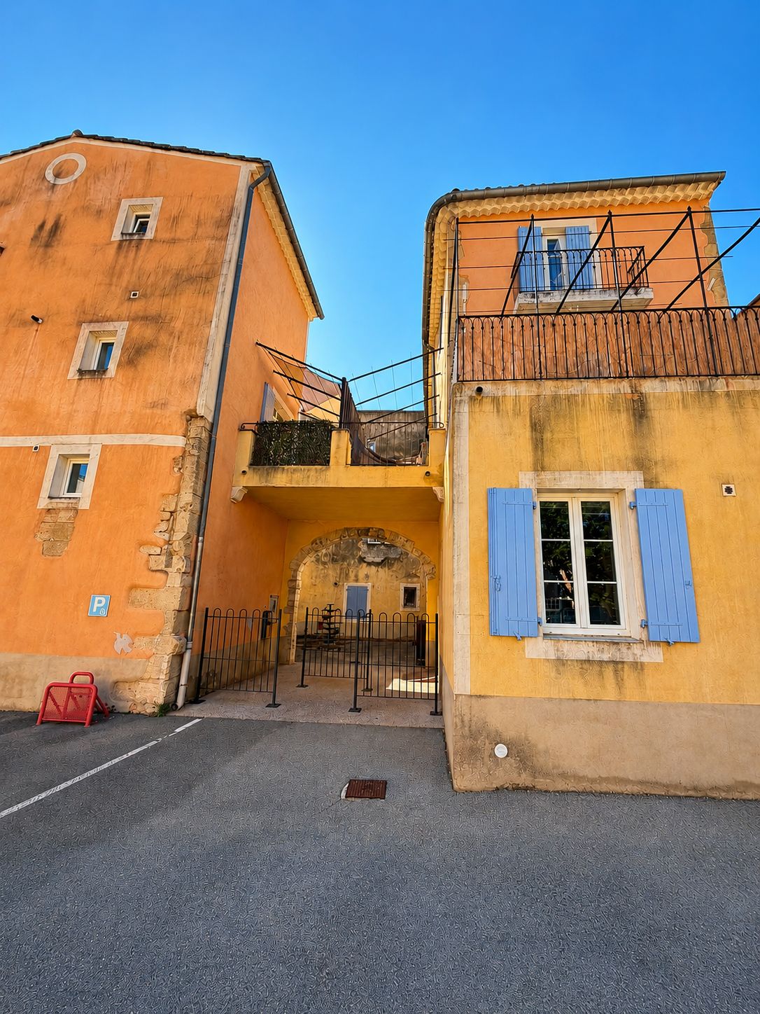 Une vue de rue avec un immeuble doté d’un balcon et d’une porte surmontée d’un arc en pierre.
