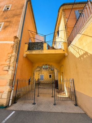 A narrow alleyway with a metal gate, a stone wall on the left, and a yellow building with a balcony on the right. - City-center gem with air conditioning and private parking (Cavaillon)