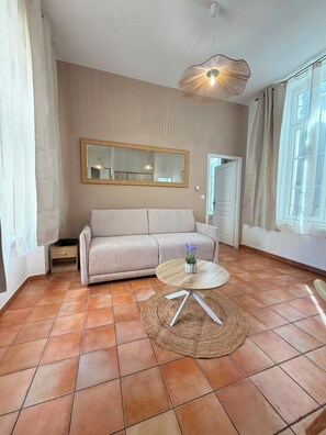 Un salon comprenant un canapé, une table ronde avec un tapis, un luminaire suspendu et un grand miroir au mur.