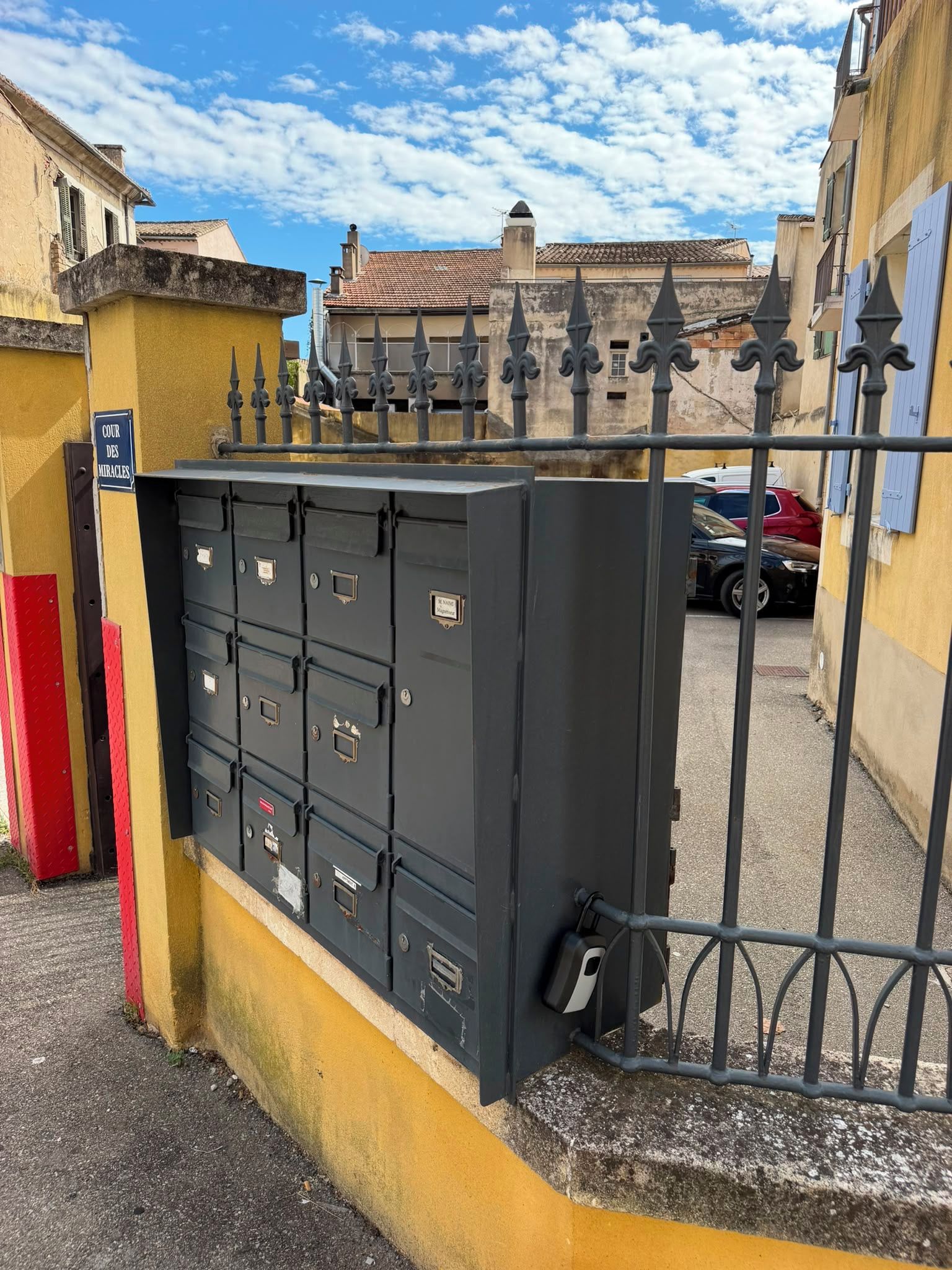 A metal security gate with a yellow wall and a sign reading 'COUR DES MIRACLES'.