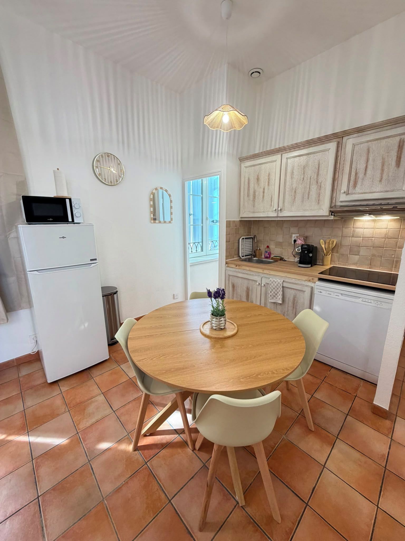 Cozinha compacta com mesa redonda de madeira, armários brancos e painel de azulejos.