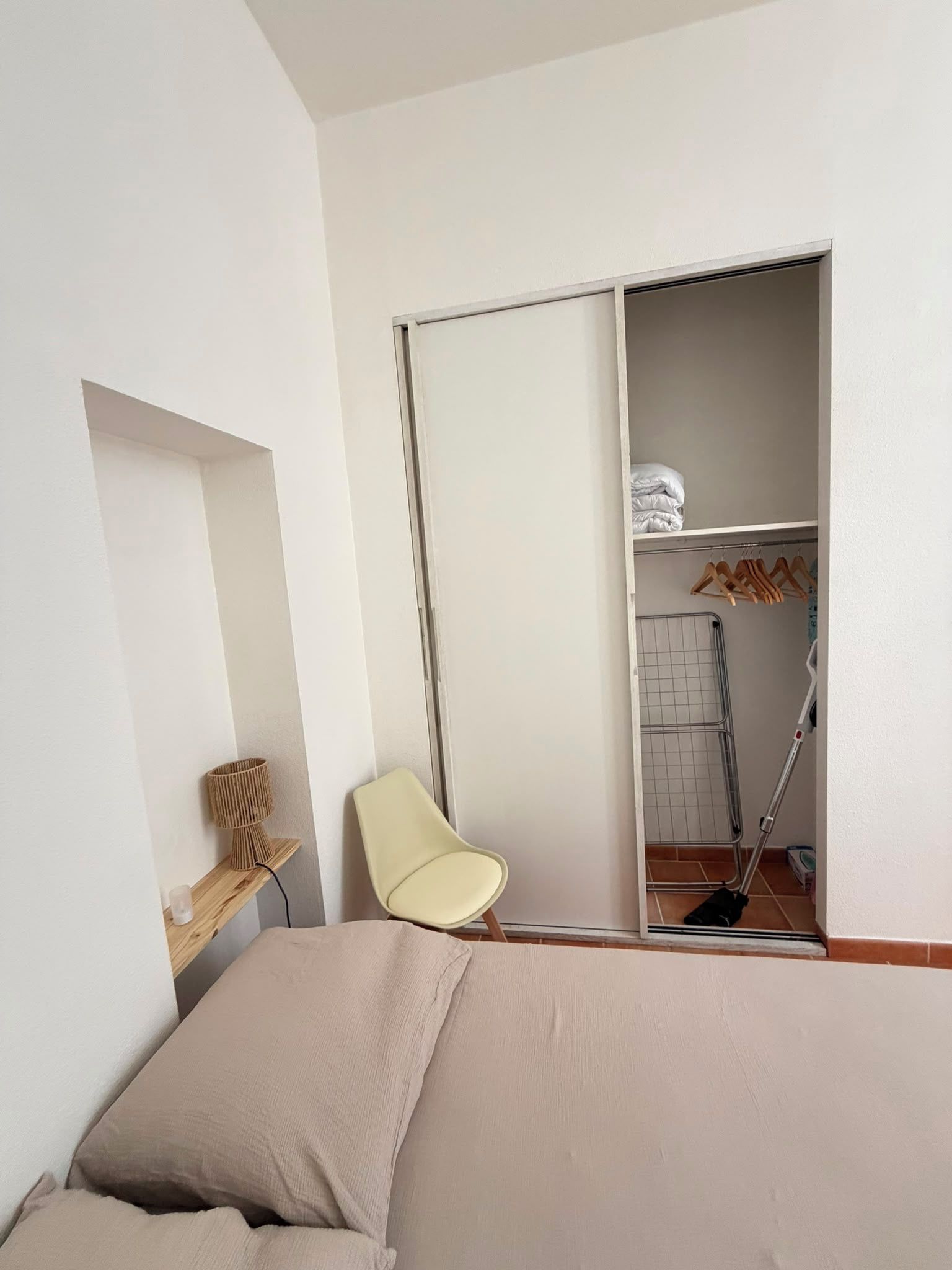 Quarto com cama, cadeira, guarda-roupa e uma pequena mesa.
