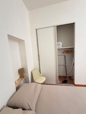 Un dormitorio con cama, una silla, un armario y una mesita.