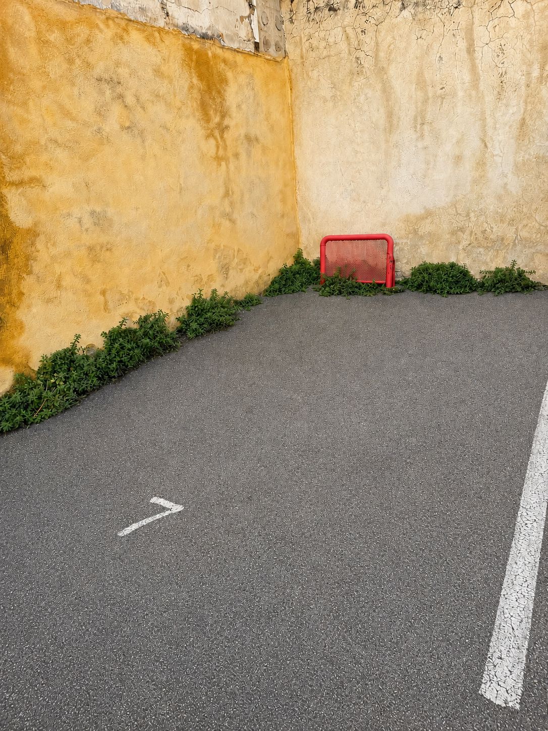 Uma área pavimentada com um objeto vermelho, possivelmente uma lixeira, e uma linha branca demarcando.