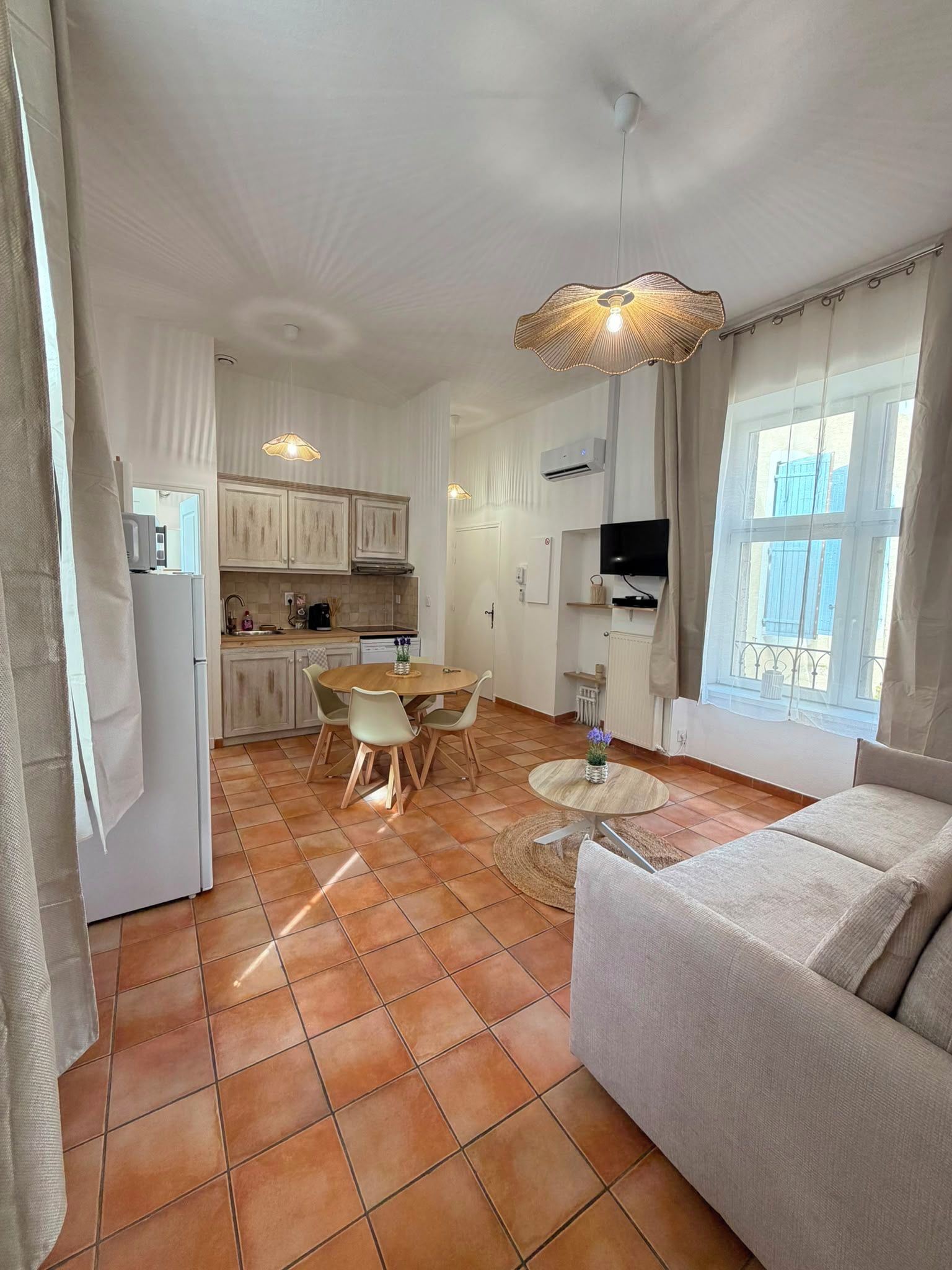 Une cuisine moderne avec des meubles blancs, une table à manger avec des chaises, un canapé et un téléviseur fixé au mur.