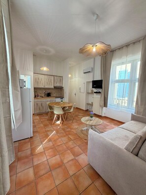 Une cuisine moderne avec des meubles blancs, une table à manger avec des chaises, un canapé et un téléviseur fixé au mur.