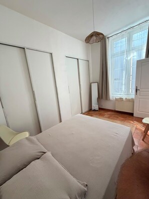 A bedroom with a bed, a chair, a wardrobe, a mirror, and a window with curtains. - City-center gem with air conditioning and private parking (Cavaillon)