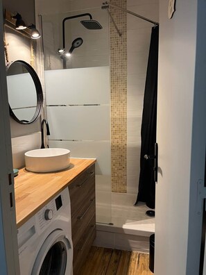 Ein kleines Badezimmer mit Waschbecken, Spiegel und Duschbereich.