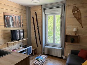 Ein gemütliches Wohnzimmer mit Fernseher, Skiern, einem Fenster und einer Heizung.